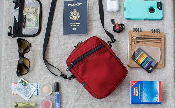 Everyday Cubelet with items around it that could fit inside: passport, phone, sunglasses, advil, makeup, notebook, italian dictionary.